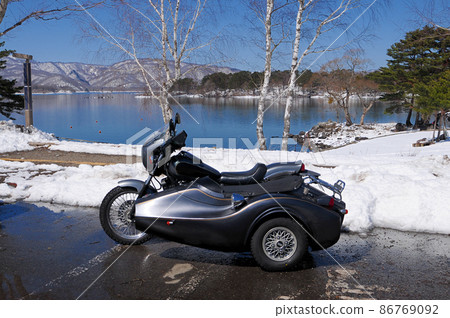 A sidecar standing on the shore of a lake with residual snow 86769092