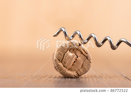 Close-up of a corkscrew on top of a wine cork on a wooden surface. Close-up of a corkscrew on top of a wine cork on a wooden surface. 86772522
