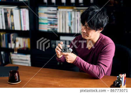 A man playing with his hobby camera in his study 86773071