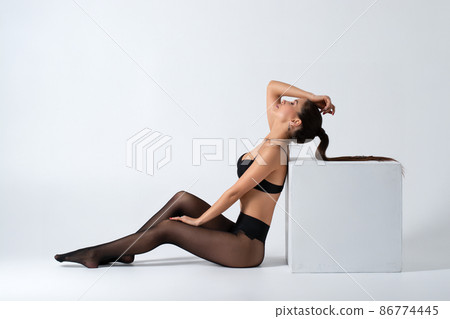 a brunette girl in black lingerie and tights on a white background.copy space. a brunette girl in black lingerie and tights on a white background.copy space. 86774445