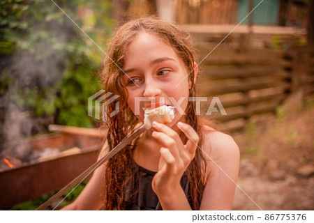 Food in nature. A teenage girl eats marshmallow roasted on a fire in the forest. Food in nature. A teenage girl eats marshmallow roasted on a fire in the forest. 86775376