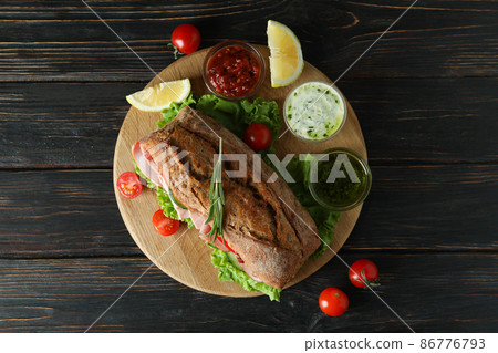 Board with ciabatta sandwich and ingredients on wooden table 86776793