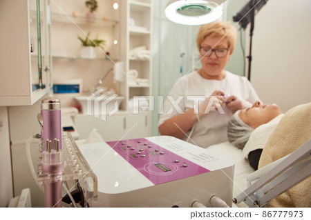 Beautician using facial multifunction machine in cosmetology clinic Beautician using facial multifunction machine in cosmetology clinic 86777973