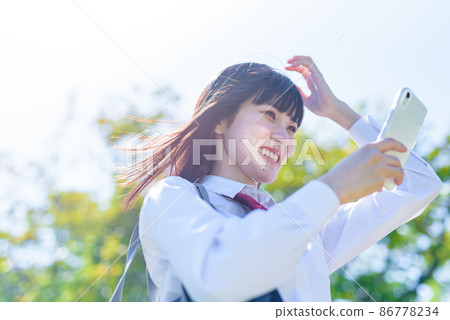 High school girl app SNS mobile phone smile to fix hairstyle with smartphone camera function in a beautiful fresh green park High school girl app SNS mobile phone smile to fix hairstyle with smartphone camera function in a beautiful fresh green park 86778234
