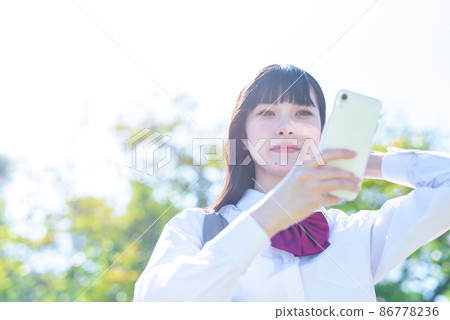 High school girl app SNS mobile phone smile to fix hairstyle with smartphone camera function in a beautiful fresh green park High school girl app SNS mobile phone smile to fix hairstyle with smartphone camera function in a beautiful fresh green park 86778236