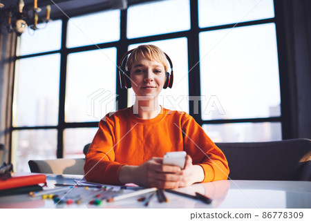 Young designer listening to song using smartphone working on creative project Young designer listening to song using smartphone working on creative project 86778309
