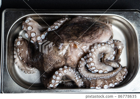 raw octopus, ready to cook a dish in an iron plate on a black background raw octopus, ready to cook a dish in an iron plate on a black background 86778635