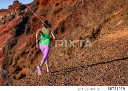 Trail runner woman ultra running uphill on volcano mountainside. Female athlete jogging in colorful activewear training hiit workout woman training outdoors Trail runner woman ultra running uphill on volcano mountainside. Female athlete jogging in colorful activewear training hiit workout woman training outdoors 86781959