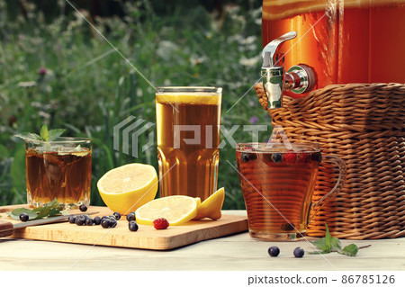 Homemade mushroom kombucha drink in a jar with a tap and in glasses with mint, berries and lemon on a wooden table 86785126