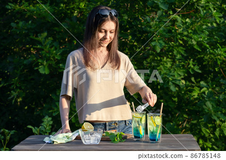 Girl makes summer refreshing cocktails blue lagoon. Process of adding ice cubes to glasses Girl makes summer refreshing cocktails blue lagoon. Process of adding ice cubes to glasses 86785148
