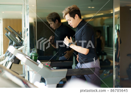 Active Asian sportsman making a cardio exercise by running on the treadmill machine in a fitness or gym, healthy sport man doing a cardio workout. Active Asian sportsman making a cardio exercise by running on the treadmill machine in a fitness or gym, healthy sport man doing a cardio workout. 86785645