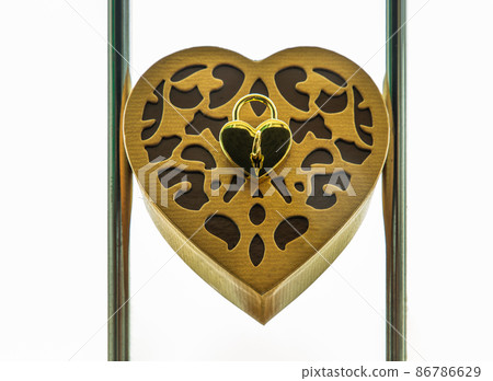 Golden heart shaped love padlock and key over on Gold heart-shaped box in the frame round steel bars. 86786629
