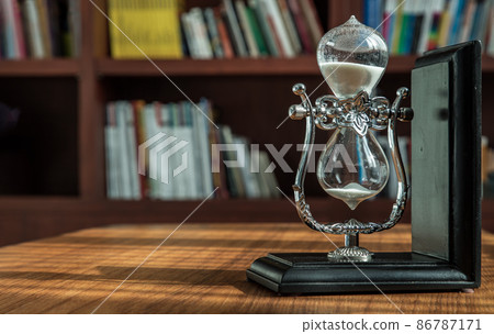 Hourglass on desk with the background of bookshelves in library. Hourglass on desk with the background of bookshelves in library. 86787171