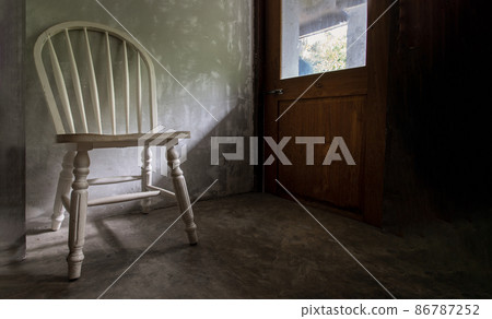 One white wooden vintage chair standing in an empty room under the light from the door. 86787252