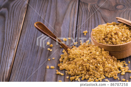Cane sugar in a wooden cup on a wooden table. 86787258