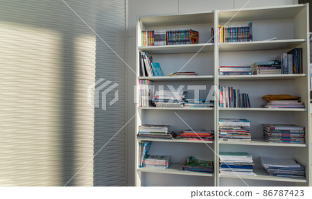 Library of shared facility at living room of home condominium. Different books are arranged on a white bookshelf. 86787423