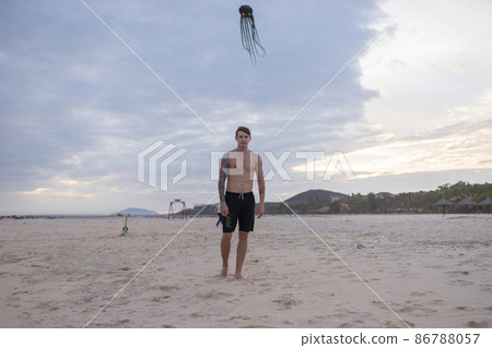Full height portrait of handsome fit bare-chested young man standing on the beach. guy with tattoo walking by the sea. High quality photo Full height portrait of handsome fit bare-chested young man standing on the beach. guy with tattoo walking by the sea. High quality photo 86788057
