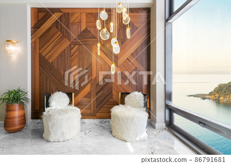 Modern white feather armless chairs, wooden plant pot, wood cladding wall, and side window revealing calm sea at sunset Modern white feather armless chairs, wooden plant pot, wood cladding wall, and side window revealing calm sea at sunset 86791681