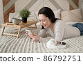 Young asian woman using smart phone surfing social media, checking news, playing mobile games or texting messages sitting on sofa. Mixed race lady spending time at home with cell gadget technology. 86792751