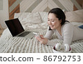 Young asian woman using smart phone surfing social media, checking news, playing mobile games or texting messages sitting on sofa. Mixed race lady spending time at home with cell gadget technology. 86792753