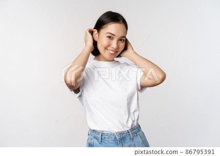 Portrait of cute, beautiful asian woman touching her new short haircut, showing hairstyle, smiling happy at camera, standing over white background Portrait of cute, beautiful asian woman touching her new short haircut, showing hairstyle, smiling happy at camera, standing over white background 86795391