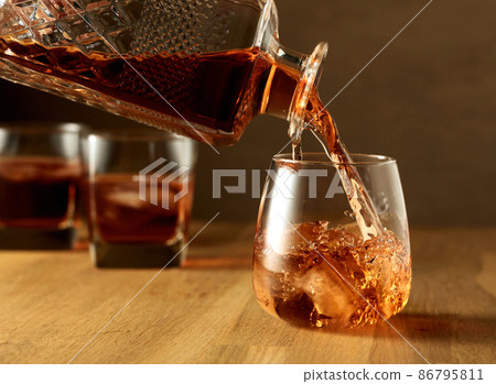 Whiskey is poured into a dammed glass with ice. Whiskey is poured into a dammed glass with ice. 86795811