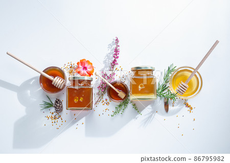 Composition of honey jars with honey sticks ,flowers and bee pollen on white background Composition of honey jars with honey sticks ,flowers and bee pollen on white background 86795982