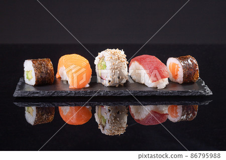 Assorted sushi served on slate plate on dark background. Japanese food. Assorted sushi served on slate plate on dark background. Japanese food. 86795988