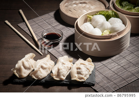 Dim sum in bamboo steamer and gyozas with soya sauce on dark background. 86795995