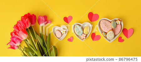 Sweets, pastry, gingerbread cookies for Easter table. Easter eggs heart shaped decor plate, pink tulips on yellow background top view copy space, spring seasonal holiday banner for site, flyer, coupon Sweets, pastry, gingerbread cookies for Easter table. Easter eggs heart shaped decor plate, pink tulips on yellow background top view copy space, spring seasonal holiday banner for site, flyer, coupon 86796475