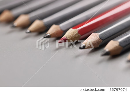Pencils tips put on grey surface in strict order, red one among black pens Pencils tips put on grey surface in strict order, red one among black pens 86797074