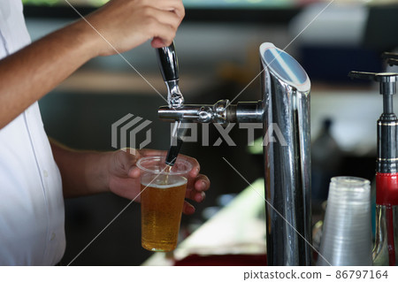 Bartender pouring beer from faucet machine in to big plastic glass Bartender pouring beer from faucet machine in to big plastic glass 86797164
