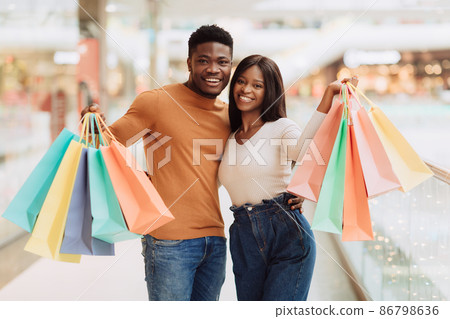 Beautiful black couple holding shopping bags looking at camera Beautiful black couple holding shopping bags looking at camera 86798636