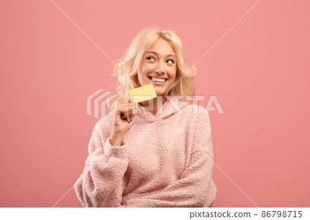 Unlimited shopping concept. Happy lady holding credit card and dreaming, thinking what to buy, pink studio background 86798715