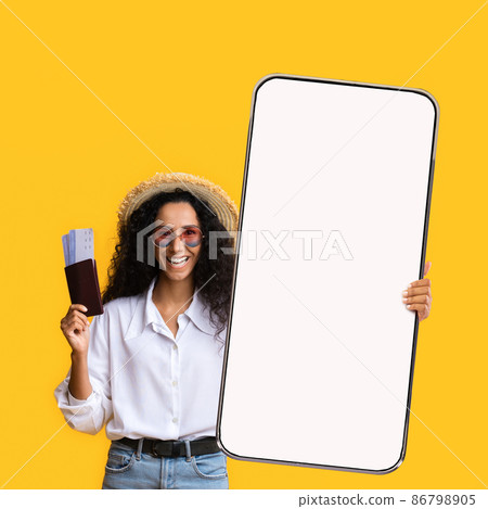 Happy hispanic lady tourist holding passport with tickets and showing huge smartphone with blank screen for mockup Happy hispanic lady tourist holding passport with tickets and showing huge smartphone with blank screen for mockup 86798905