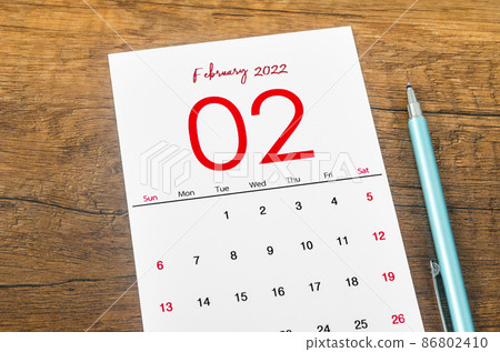 February 2022 calendar with pen on wooden table. 86802410