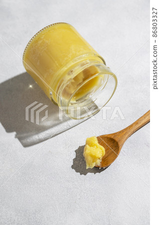 Ghee in a glass jar made with sunflower oil on a light background, copy space for text. Hard light. Ghee in a glass jar made with sunflower oil on a light background, copy space for text. Hard light. 86803327