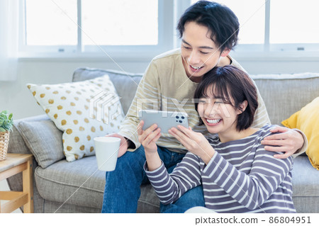 A young couple relaxing while looking at a smartphone on the sofa 86804951
