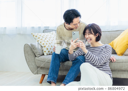 A young couple relaxing while looking at a smartphone on the sofa A young couple relaxing while looking at a smartphone on the sofa 86804972