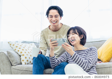 一對年輕夫婦一邊看著沙發上的智能手機一邊放鬆 一對年輕夫婦一邊看著沙發上的智能手機一邊放鬆 86804973