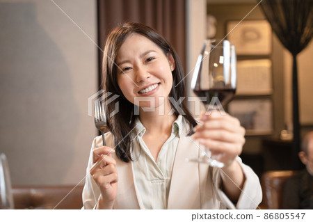 A woman toasting with red wine at a restaurant 86805547