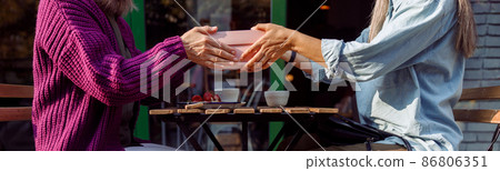 Senior women friends hold gift box above table on outdoors cafe terrace 86806351