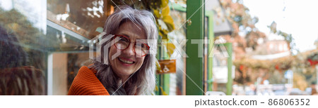 Positive mature woman with glasses and laptop holds cup ositting near cafe Positive mature woman with glasses and laptop holds cup ositting near cafe 86806352