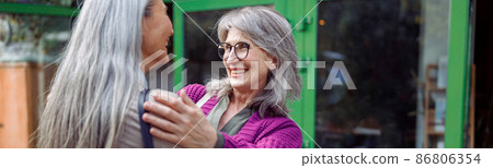 Smiling mature woman embraces female friend meeting on modern city street Smiling mature woman embraces female friend meeting on modern city street 86806354