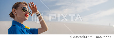 Portrait of elegant air stewardess in blue uniform and sunglasses holding hand near her head and looking far away, standing on airstair on a daytime Portrait of elegant air stewardess in blue uniform and sunglasses holding hand near her head and looking far away, standing on airstair on a daytime 86806367