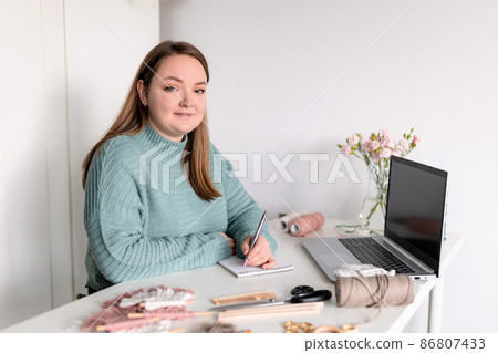 Young stylish woman using laptop at home, writing to do list. Female hobby. Working on research project online concept. Handmade macrame shop Young stylish woman using laptop at home, writing to do list. Female hobby. Working on research project online concept. Handmade macrame shop 86807433