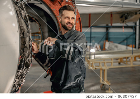 Cheerful male mechanic repairing aircraft in hangar 86807457