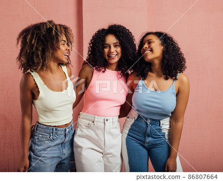 Three cheerful women with curly hair having fun together while standing at a pink wall Three cheerful women with curly hair having fun together while standing at a pink wall 86807664