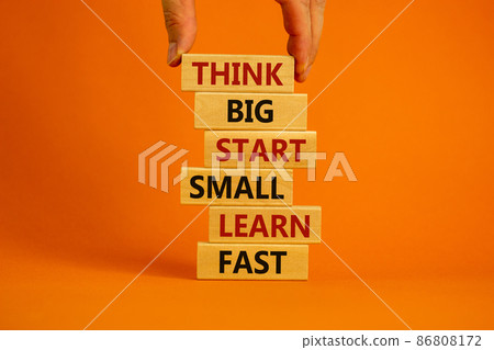 Think big start small symbol. Words 'Think big start small learn fast' on wooden blocks on a beautiful orange background. Businessman hand. Business, motivational and think big start small concept. Think big start small symbol. Words 'Think big start small learn fast' on wooden blocks on a beautiful orange background. Businessman hand. Business, motivational and think big start small concept. 86808172