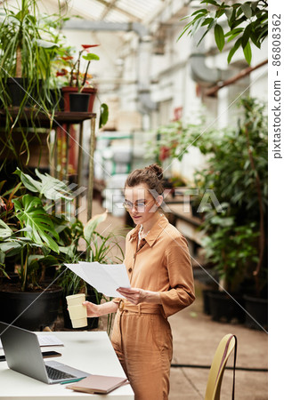Young female accountant of contemporary orangerie or florist shop Young female accountant of contemporary orangerie or florist shop 86808362